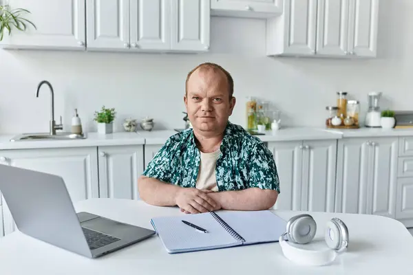 Homme avec inclusivité en chemise florale à table blanche avec ordinateur portable, ordinateur portable, stylo. — Photo de stock