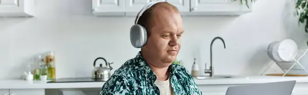 A man with inclusivity wearing headphones works on a laptop in his kitchen. — Stock Photo