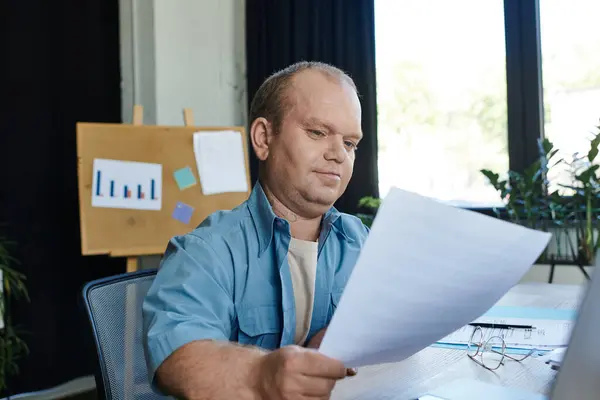 A man with inclusivity sits at a desk, reviewing documents in a well-lit home office. — Stock Photo
