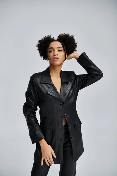 Uma jovem mulher elegante em um blazer de couro preto posa contra um pano de fundo cinza, apresentando um olhar ousado e confiante. — Fotografia de Stock