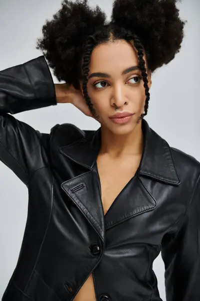 A stylish young African American woman poses in a black leather jacket against a grey background. — Stock Photo