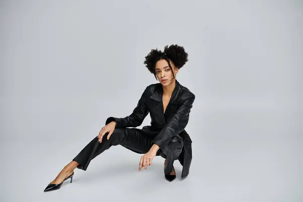 A stylish young African American woman poses in a black leather outfit against a grey background. — Stock Photo