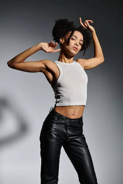 A stylish young African American woman in a white tank top poses against a gray background. — Stock Photo
