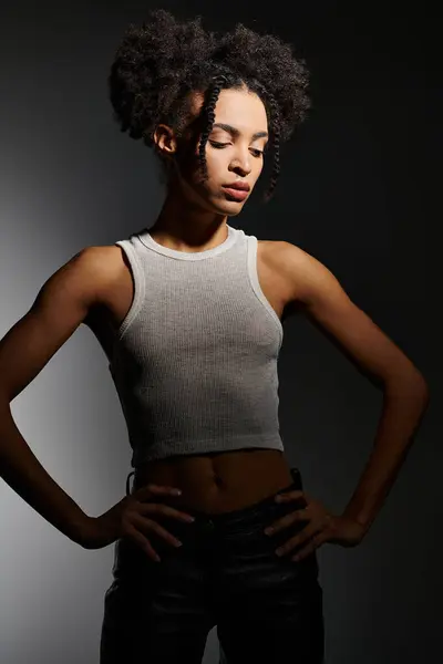 A young African American woman poses in a white tank top against a grey backdrop. — Stock Photo