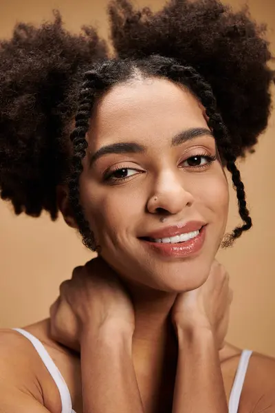 Uma jovem mulher negra com um sorriso quente e um belo penteado olha diretamente para a câmera contra um pano de fundo bege. — Fotografia de Stock