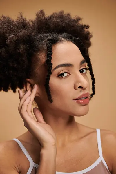 Uma jovem afro-americana com a pele brilhando, posa contra um fundo bege. — Fotografia de Stock