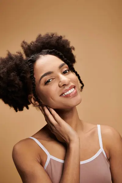 Uma bela jovem afro-americana com o cabelo em dois pães sorri brilhantemente enquanto posa contra um pano de fundo bege. — Fotografia de Stock