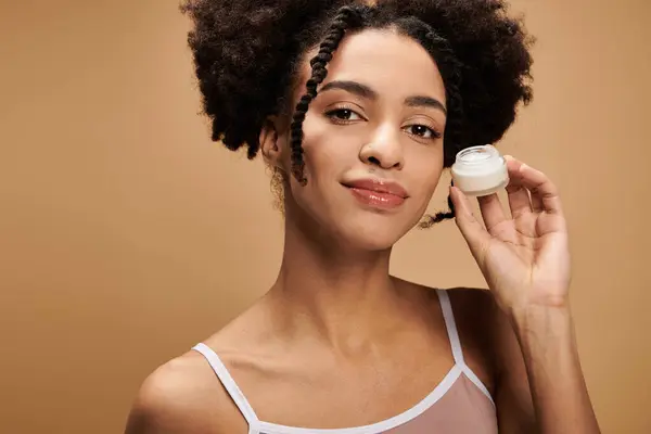 Uma jovem afro-americana com pele bonita segura um frasco de creme, mostrando sua beleza natural. — Fotografia de Stock