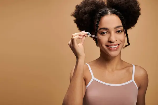 Uma bela jovem afro-americana sorri enquanto aplica soro ao rosto. — Fotografia de Stock