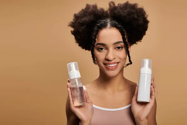 A young African American woman with a radiant smile holds two bottles of face wash, highlighting her natural beauty and confidence. — Stock Photo