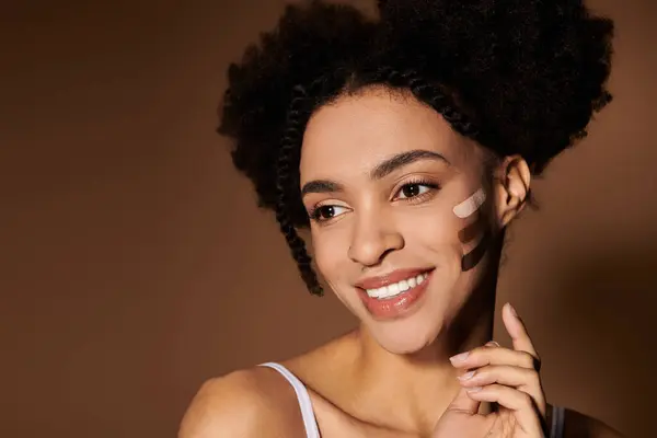 A young woman with a bright smile shows off different skin tone swatches on her cheek. — Stock Photo