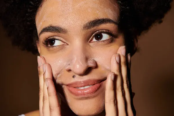 A young woman with dark skin gently applies a cleansing product to her face, showcasing the beauty of diversity. — Stock Photo