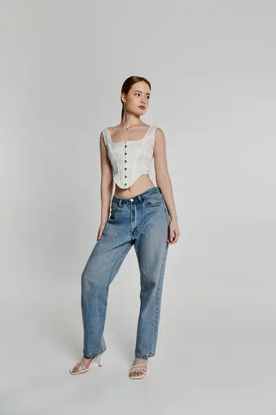 Una giovane donna in un corsetto bianco e jeans blu posa su uno sfondo bianco. — Foto stock