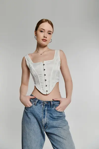A young woman poses in a white corset and blue jeans against a simple background. — Stock Photo
