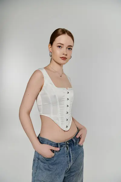 A young woman with red hair poses in a white corset and jeans. — Stock Photo