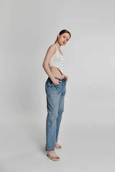 A young woman poses in a white corset and jeans against a white backdrop. — Stock Photo