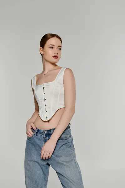 A young woman poses confidently, wearing a white corset and denim jeans. — Stock Photo