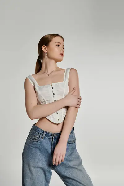 A young woman poses in a white corset and blue jeans against a white backdrop. — Stock Photo