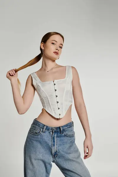 A young woman poses confidently in a white corset and blue jeans against a light background. — Stock Photo