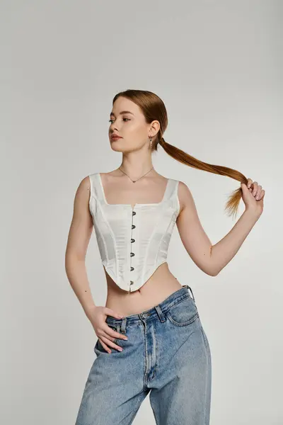 Una giovane donna posa con i capelli tirati indietro in una coda di cavallo, indossando un corsetto bianco e jeans blu. — Foto stock