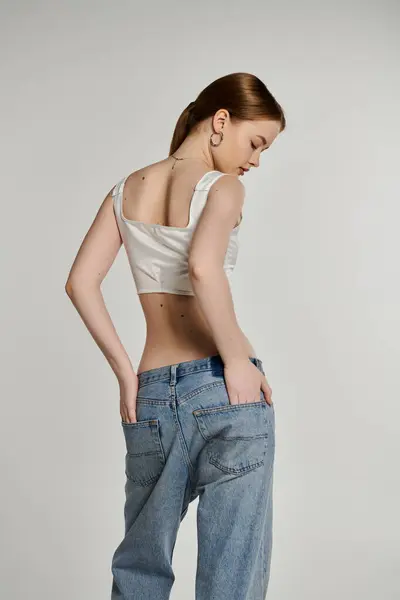 Молодая женщина в джинсах стоит на обычном фоне с руками в карманах. — стоковое фото