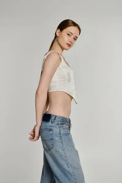 Eine junge Frau posiert vor weißem Hintergrund, trägt ein weißes Oberteil und Jeans. — Stock Photo