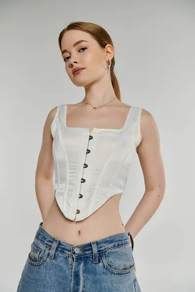 Una joven con una blusa de corsé blanco y vaqueros azules posa con una expresión confiada. — Stock Photo