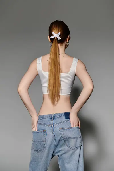 Una giovane donna con i capelli lunghi posa in un crop top bianco e jeans, guardando lontano dalla fotocamera. — Foto stock