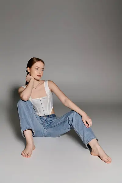 A young woman poses in a white corset and jeans against a gray backdrop. — Stock Photo