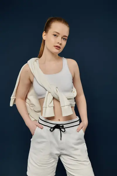 A young woman poses in white athletic clothing against a vibrant blue backdrop. — Stock Photo