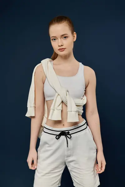 A young woman wearing a white tank top and shorts poses in front of a deep blue background. — Stock Photo