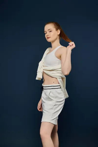 Una giovane donna posa in pantaloncini bianchi e una canotta bianca su uno sfondo blu vibrante. — Foto stock