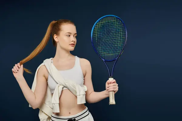 Una giovane donna in canotta bianca tiene una racchetta da tennis davanti a uno sfondo blu. — Foto stock