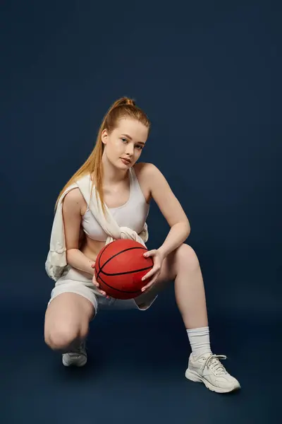 A stylish, active young woman holding a basketball against a striking blue backdrop. — Stock Photo