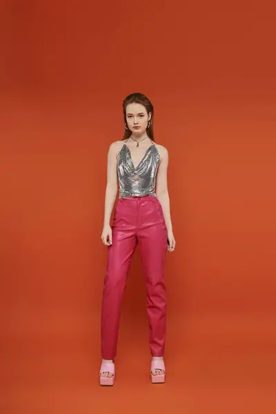 Молода жінка в срібному верхньому і рожевому штанях позує на яскравому помаранчевому фоні. — стокове фото