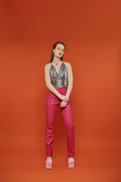 Woman in chainmail top, pink pants, and sandals poses in orange room. — Stock Photo