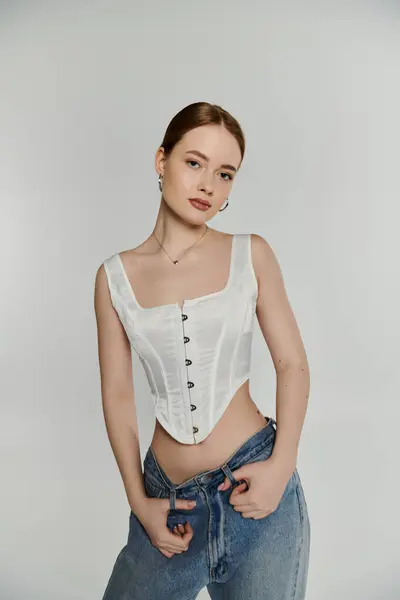 A young woman poses confidently in a white corset against a simple backdrop. — Stock Photo