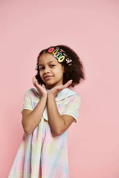 Una linda chica afroamericana con pinzas para el cabello está en un vestido colorido sobre un fondo rosa. — Stock Photo