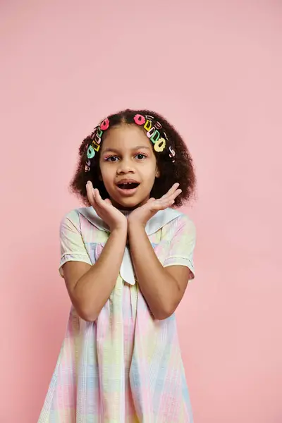 Une jeune afro-américaine avec des pinces à cheveux colorées se tient dans une robe pastel sur un fond rose. — Photo de stock