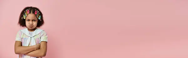 Offended African American girl with hair clips stands against a pink backdrop. — Stock Photo