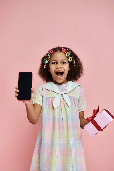 A young African American girl in a colorful dress smiles and holds a phone with a blank screen. — Stock Photo