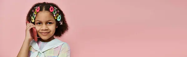 Uma jovem afro-americana com grampos de cabelo coloridos fica contra um fundo rosa, segurando um telefone rosa no ouvido e sorrindo. — Fotografia de Stock