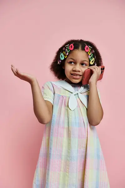 Una linda chica afroamericana con pinzas para el cabello está en un vestido de color arco iris, sonriendo a la cámara. — Stock Photo