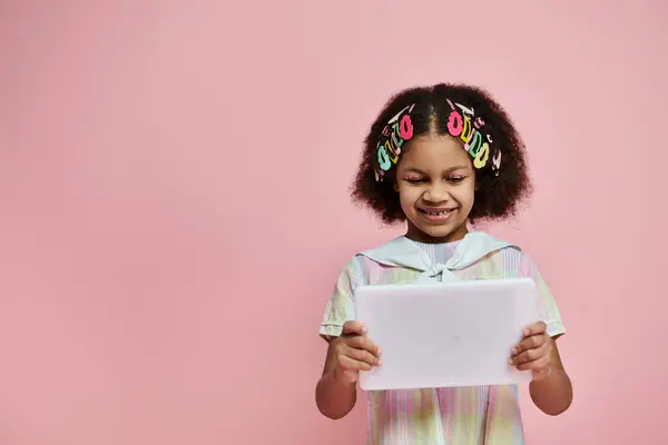 Uma jovem com clipes de cabelo coloridos sorri enquanto usa um tablet branco na frente de um fundo rosa. — Fotografia de Stock