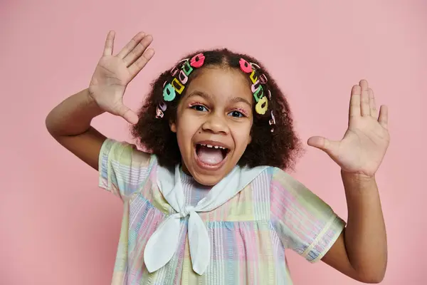 A young African American girl with colorful hair clips smiles brightly while wearing a pastel dress. — Stock Photo
