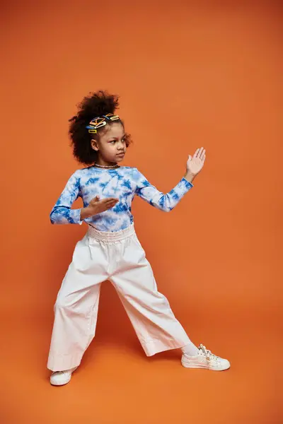 Ein stilvolles junges afroamerikanisches Mädchen mit Haarspangen posiert in einem trendigen Outfit vor orangefarbenem Hintergrund. — Stockfoto