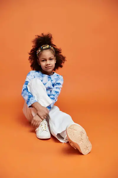 African American girl with hair clips sitting on the ground with legs crossed, lost in contemplation. — Stock Photo