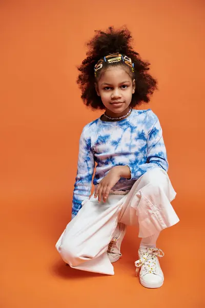 A young African American girl poses with confidence in a trendy tie-dye shirt and white pants, her hair adorned with colorful clips. — Stock Photo