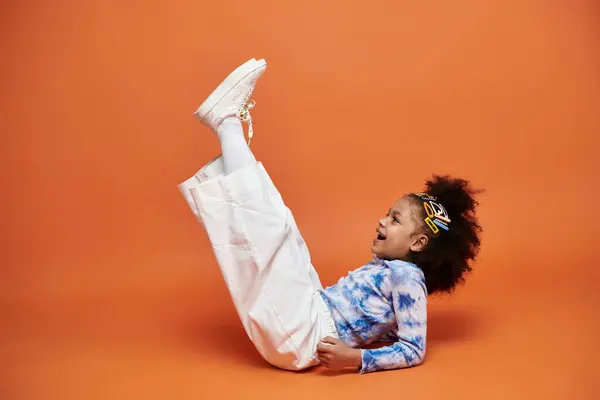 Une jeune afro-américaine dans une tenue tendance et des pinces à cheveux pose sur un fond orange. — Photo de stock