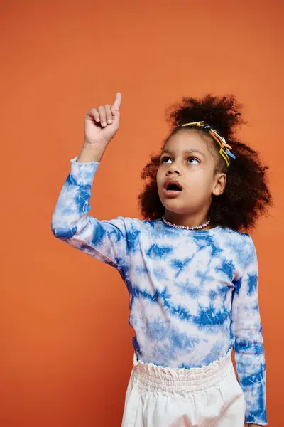 Une jeune afro-américaine avec des pinces à cheveux se tient dans une tenue à la mode sur un fond orange. — Photo de stock